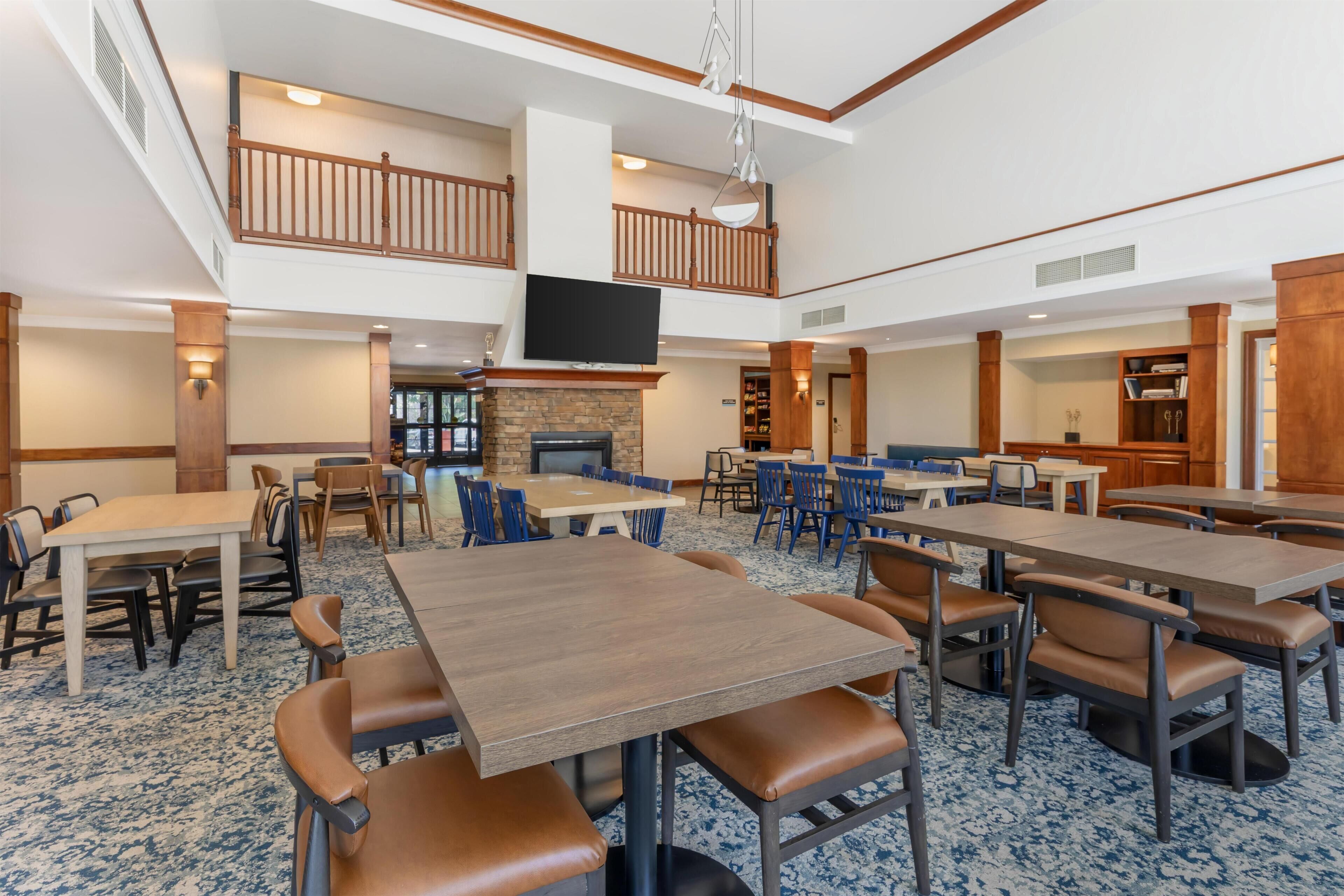 A spacious dining area with multiple tables and chairs, a fireplace, and a television mounted on the wall.