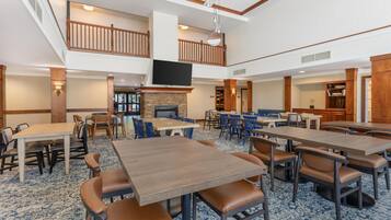 A spacious dining area with multiple tables and chairs, a fireplace, and a television mounted on the wall.