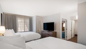 Une chambre d’hôtel avec deux lits, une télévision, une commode et une vue sur une autre chambre par une porte ouverte.