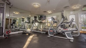 Un gimnasio con diversas máquinas de ejercicio, un espejo grande y una cinta de correr.