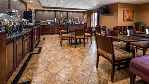 A hotel dining area with a bar, multiple tables and chairs, and a tiled floor. - Best Western Plus Midwest Inn & Suites (Salina)