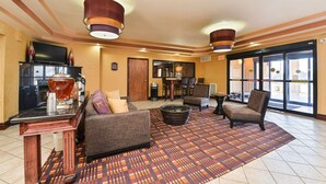 A hotel lobby with a sofa, armchairs, a coffee table, a TV, and a fireplace. - Best Western Plus Midwest Inn & Suites (Salina)