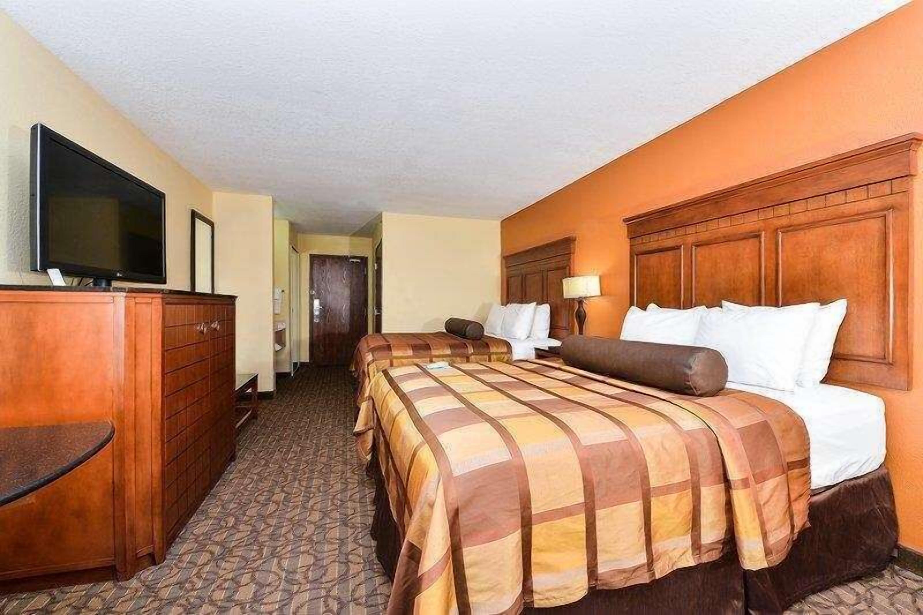 Une chambre d’hôtel avec un grand lit, un bureau avec une télévision et une tête de lit en bois.