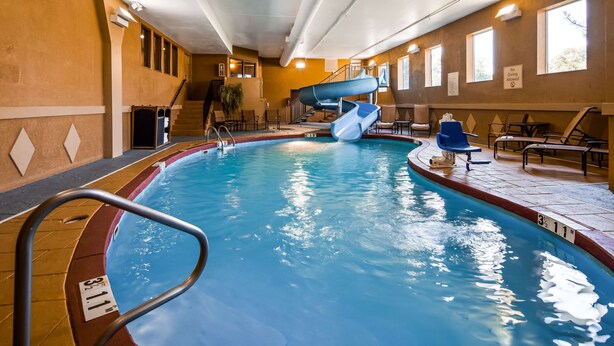 An indoor swimming pool with a slide, lounge chairs, and a staircase. - Best Western Plus Midwest Inn & Suites (Salina)
