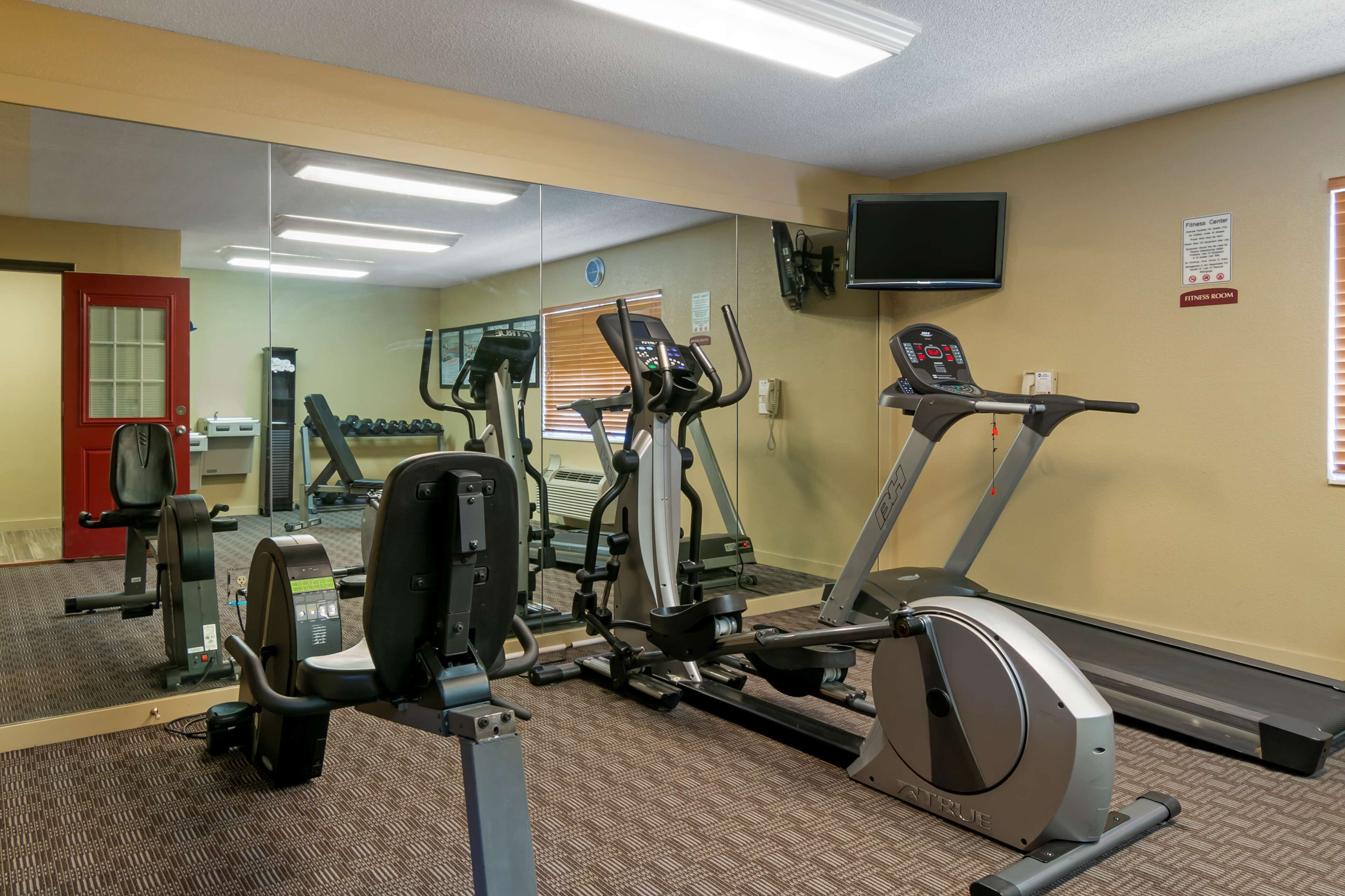 A gym with cardio machines, weight equipment, a mirror, and a TV on the wall.