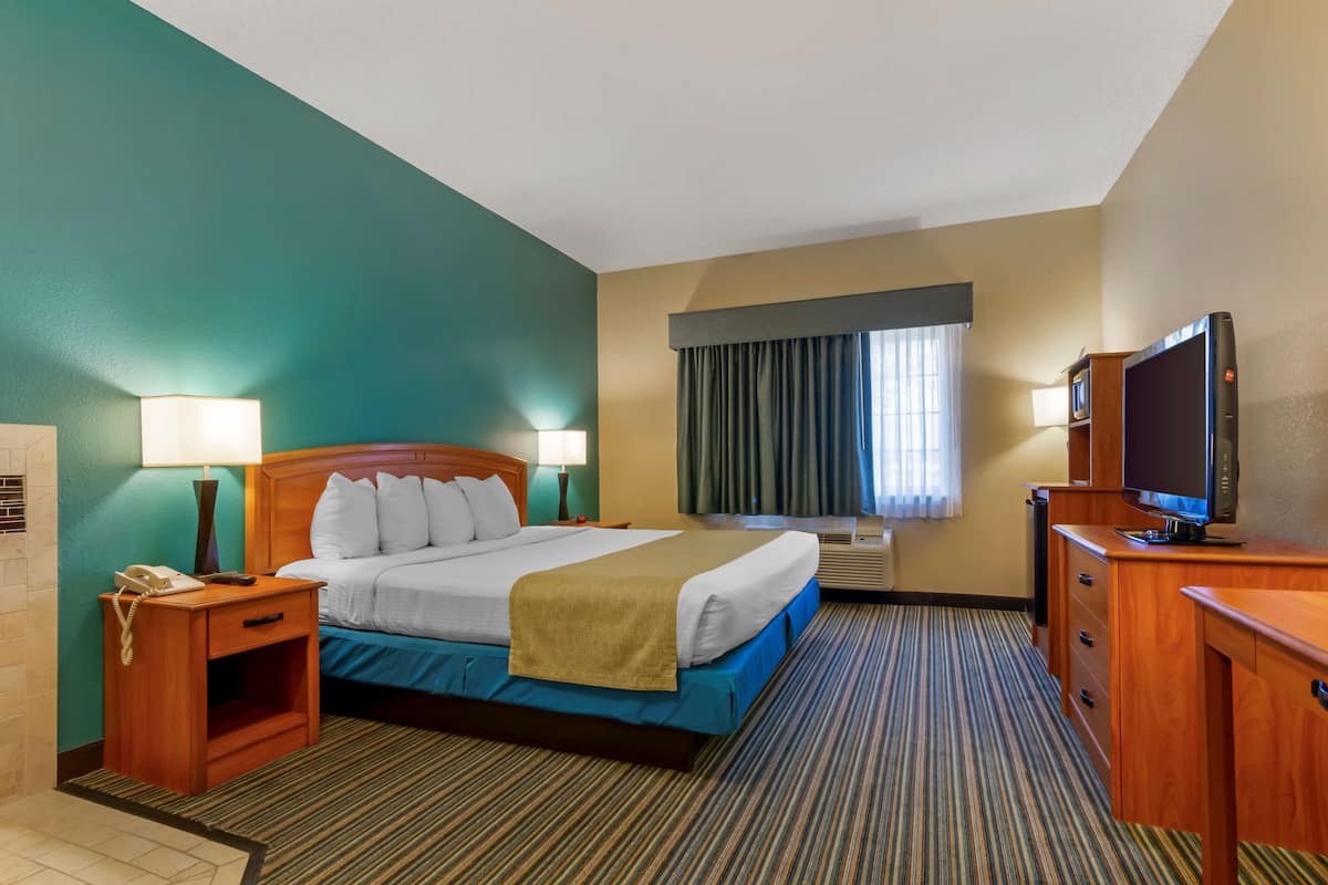 A hotel room with a bed, bedside tables, a TV, and a window with curtains.