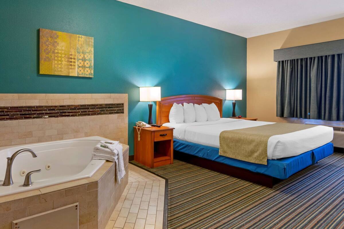 A hotel room with a large bed, a separate bathroom with a bathtub, two bedside lamps, and a wall-mounted artwork.