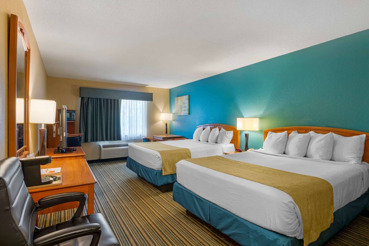 A hotel room with two beds, a desk, a chair, and a large mirror.