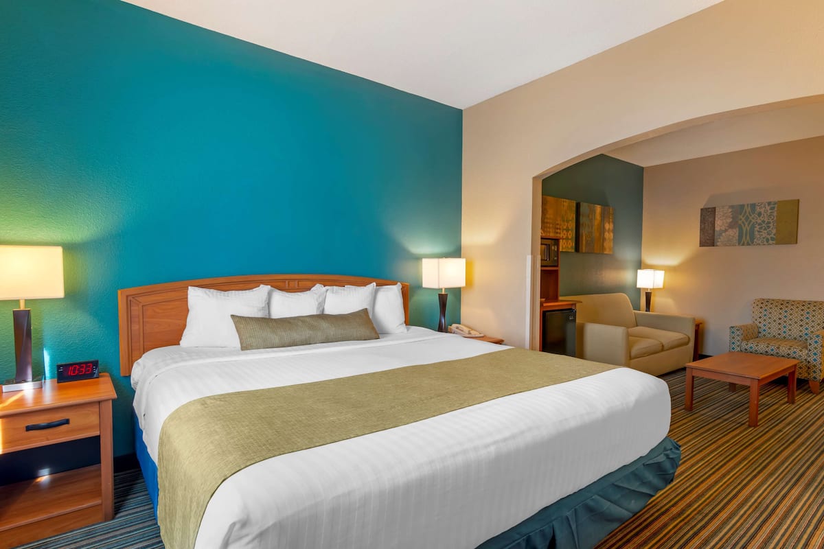 A hotel room with a large bed, two bedside tables with lamps, a chair, a desk, and a small table.