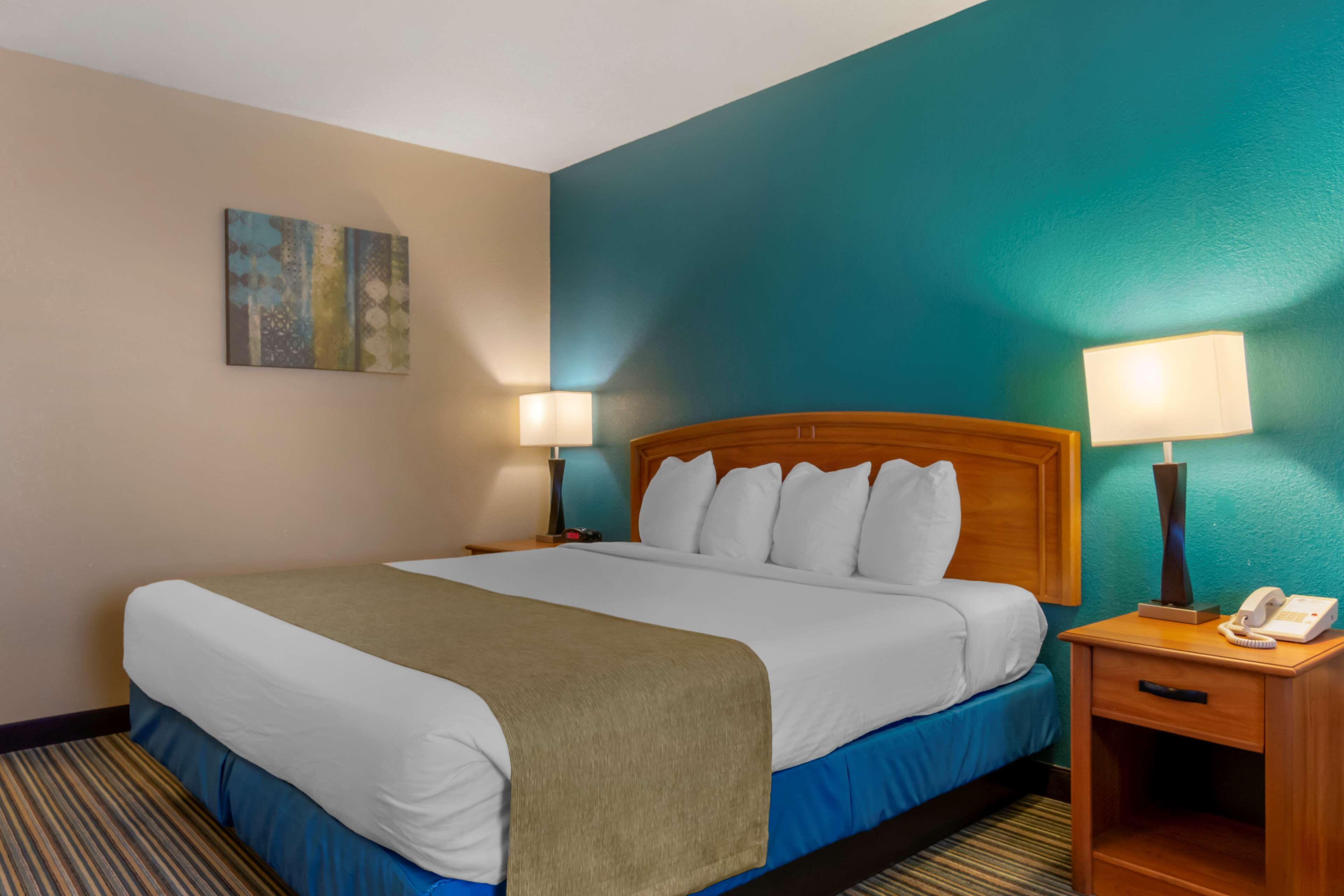 Camera d'albergo con un letto grande, due comodini con lampade, un telefono e un quadro appeso al muro.