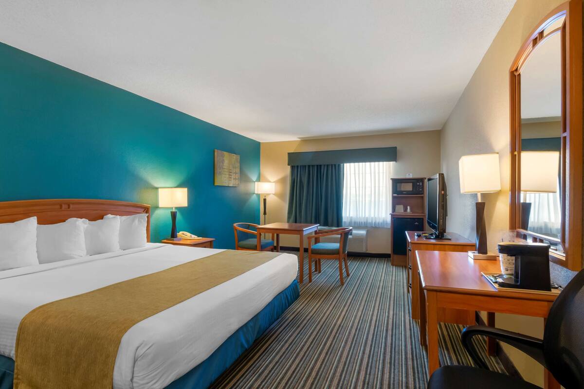 A hotel room with a large bed, a desk, a chair, a television, and a window with curtains.