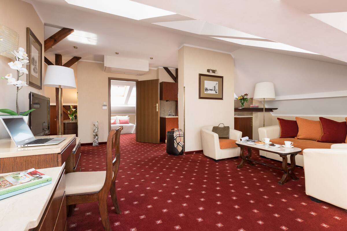 Habitación de hotel con escritorio, laptop, silla, sofá y alfombra estampada roja.