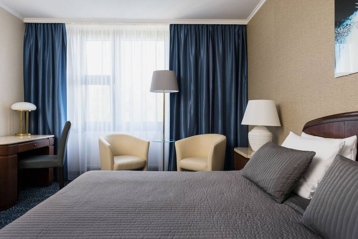 A hotel room with a large bed, two chairs, a desk, and a lamp.