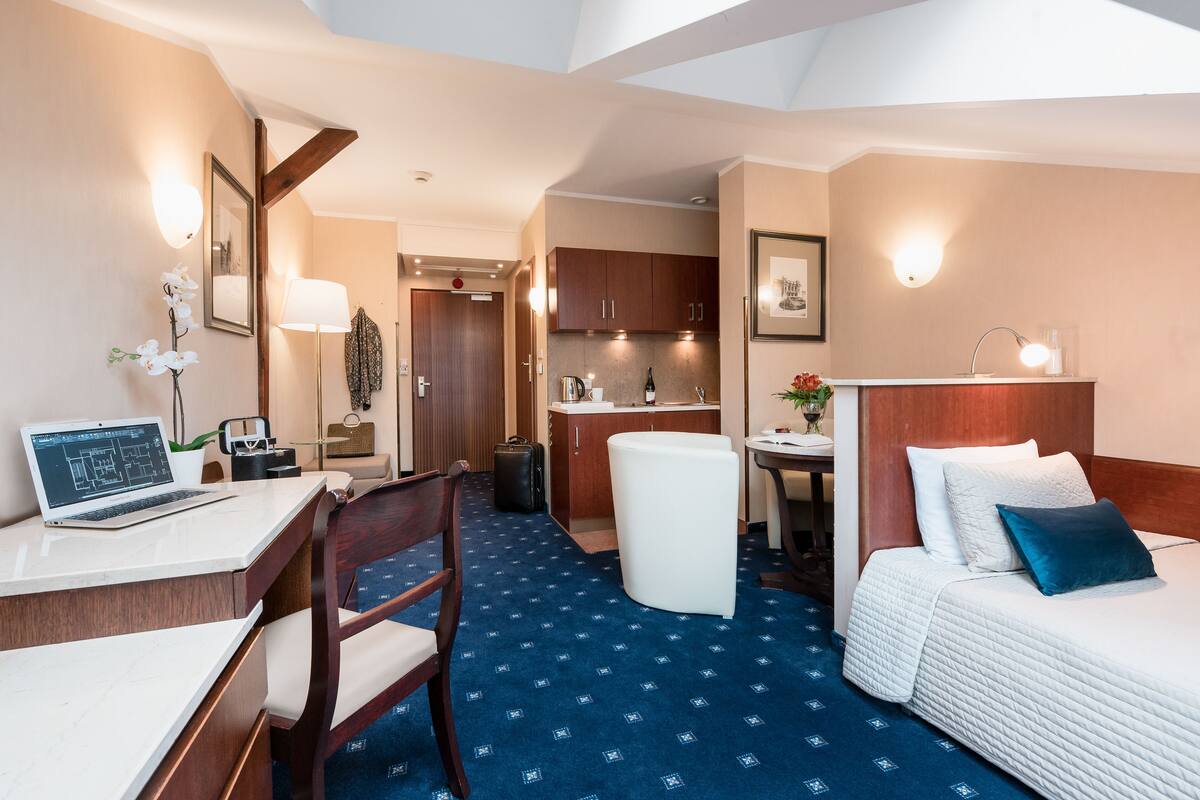 A hotel room with a desk, chair, bed, and kitchenette.