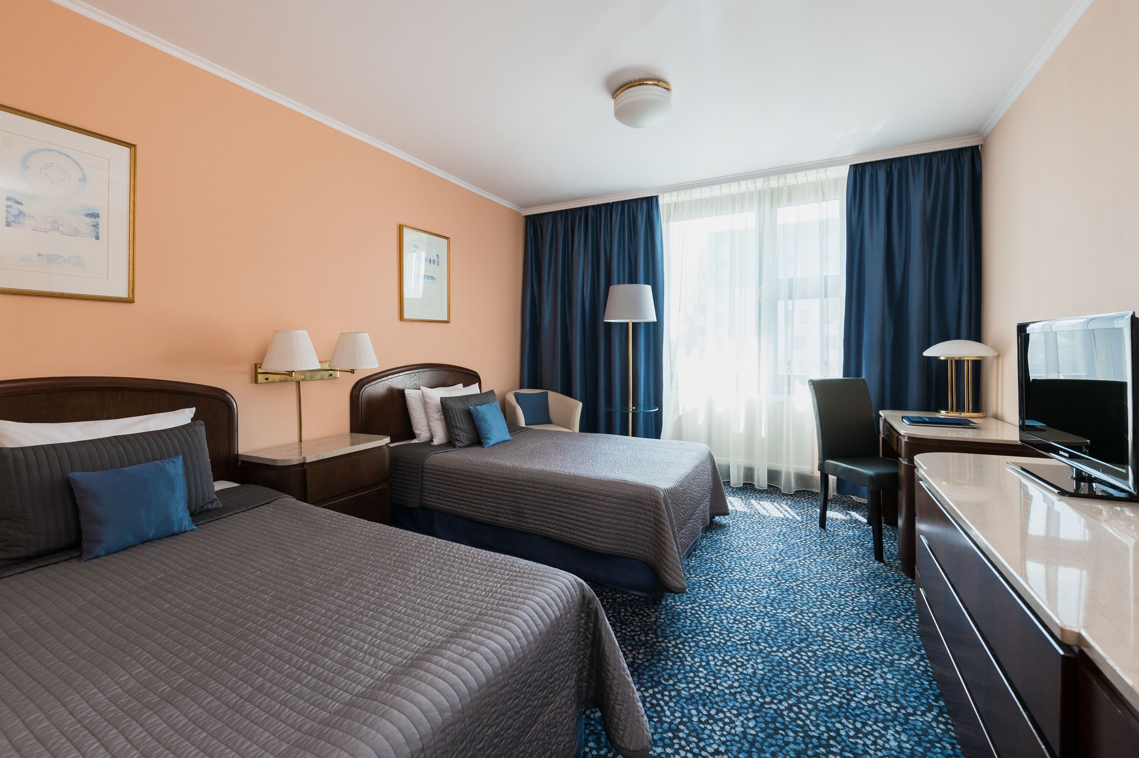 Habitación de hotel con dos camas, un escritorio, un televisor y una ventana con cortinas.