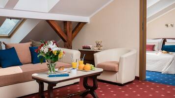 Una habitación acogedora con sofá, una mesita con un jarrón de flores, un osito de peluche y una cama con edredón azul y blanco.