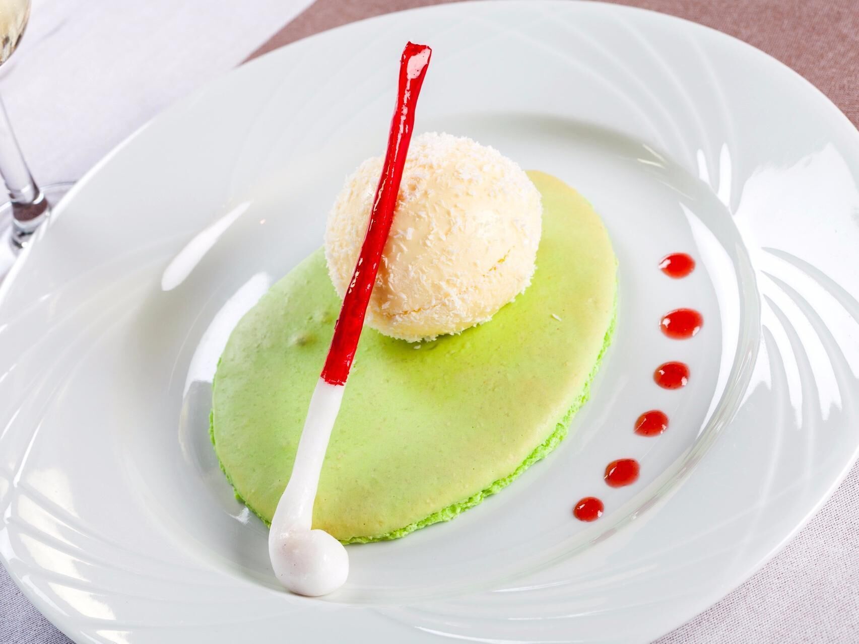 Un dessert servi dans une assiette blanche, avec une base verte, une sphère blanche sur le dessus et un élément rayé de rouge et de blanc.