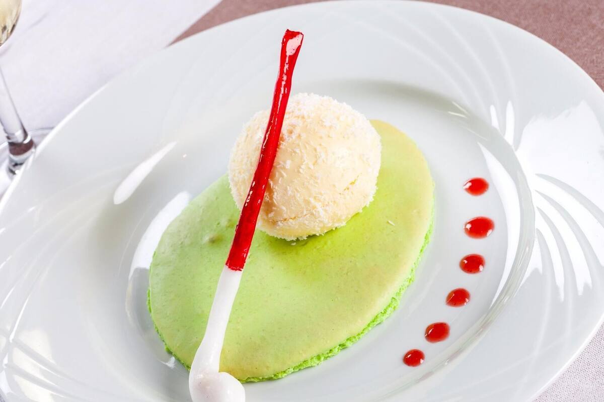 En dessert på en hvid tallerken med en grøn bund, en hvid kugle ovenpå og en rød-hvid stribet genstand.
