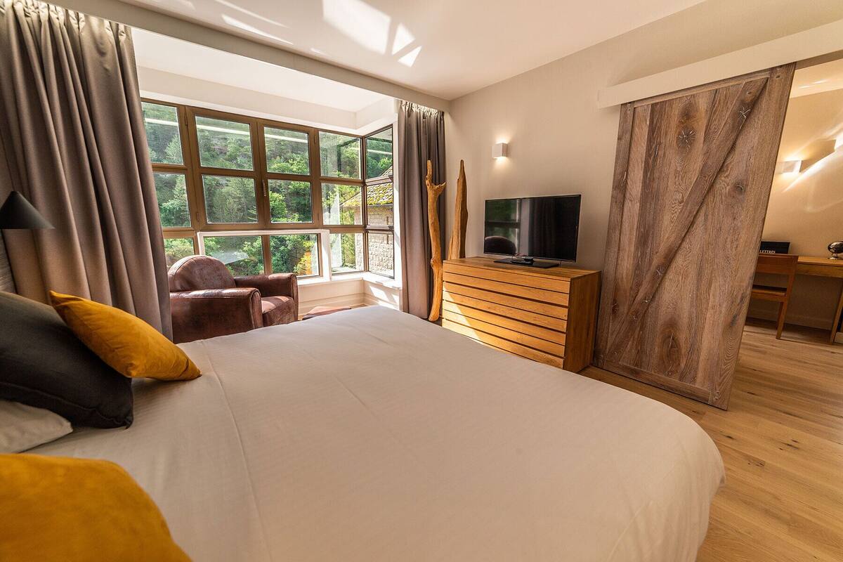 A bedroom with a large bed, a TV on a wooden dresser, a chair, and a desk.