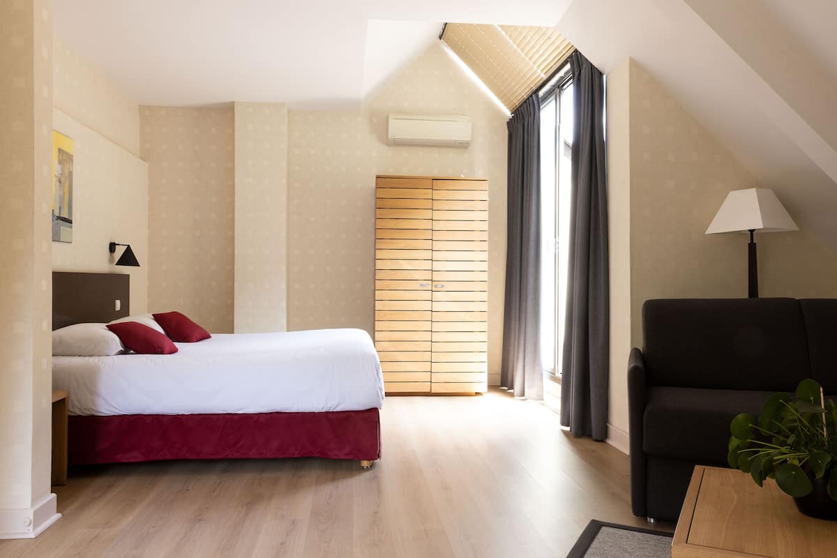 A modern bedroom with a bed, a sofa, a lamp, and a plant.
