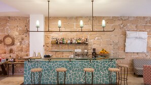 A bar area with a mosaic-tiled counter, four stools, a selection of bottles, and a stone wall backdrop. - Hotel Palau Sa Font (Palma de Mallorca)
