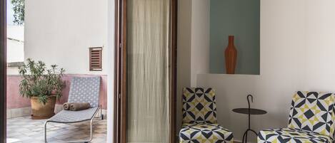 A room with a sliding glass door leading to an outdoor area with a tiled floor, a potted plant, and a cushioned chair.