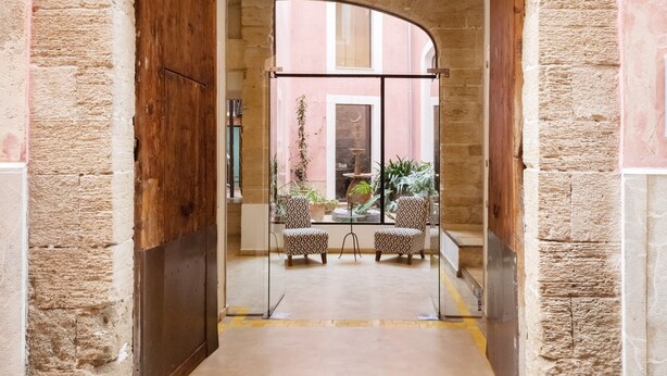 An arched doorway leading into a courtyard with two patterned chairs and a table, surrounded by potted plants. - Hotel Palau Sa Font (Palma de Mallorca)