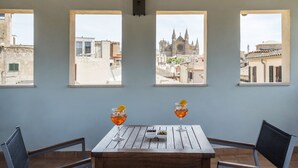 A table with two glasses of a red beverage, a small dish of olives, and a view of a historic church through three windows. - Hotel Palau Sa Font (Palma de Mallorca)