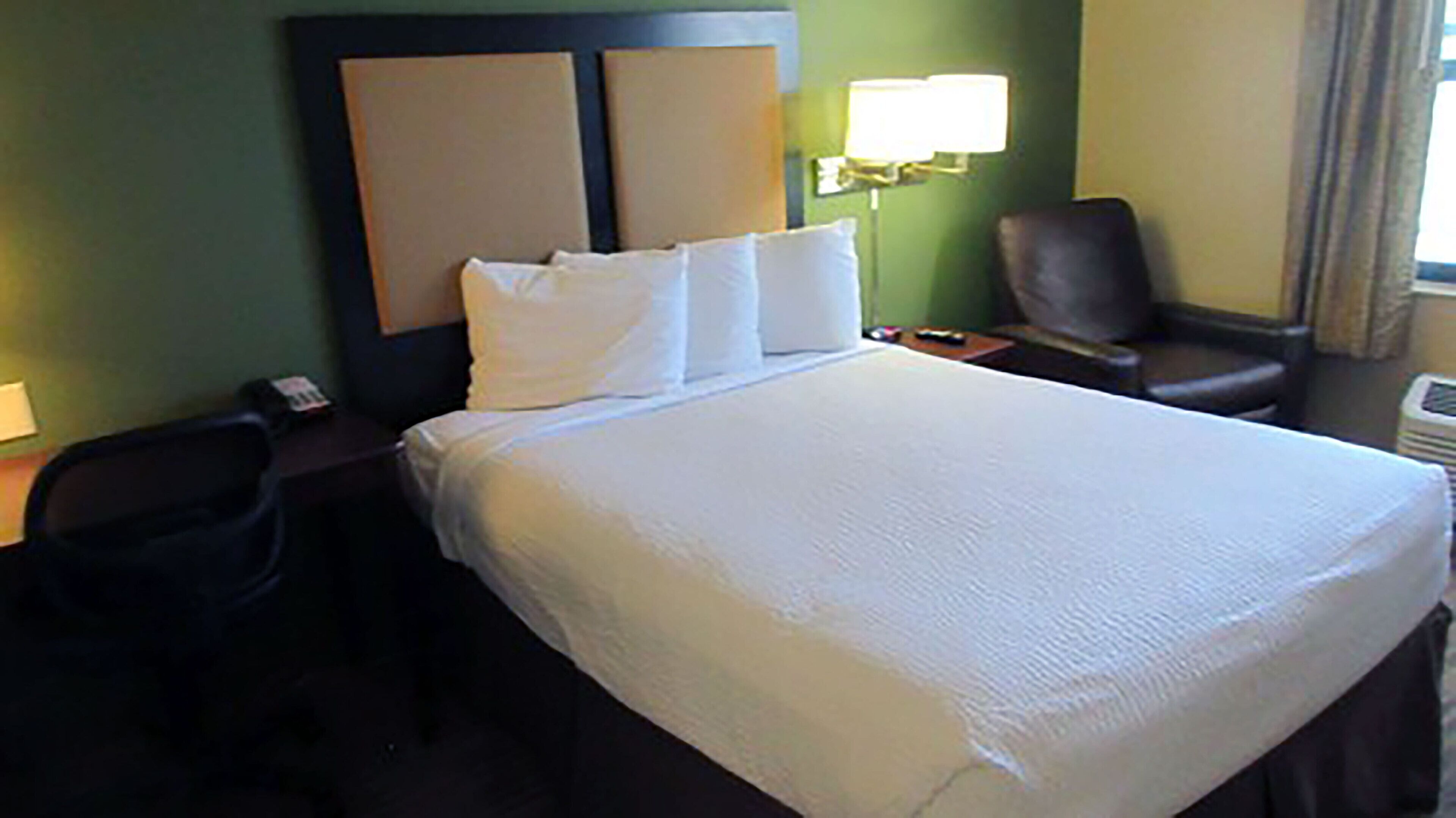 A hotel room with a large bed, a desk with a chair, a lamp, and a window with curtains.