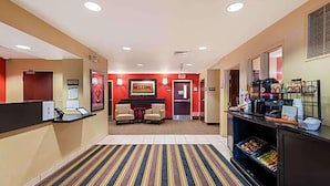A hotel lobby with a reception desk, a 'WELCOME' sign, a seating area, and a buffet counter.