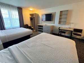 A hotel room with two beds, a desk, a chair, a TV, a wardrobe, and a window with curtains.