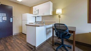 A compact kitchen with a refrigerator, microwave, and sink. There's a small dining table with a chair.