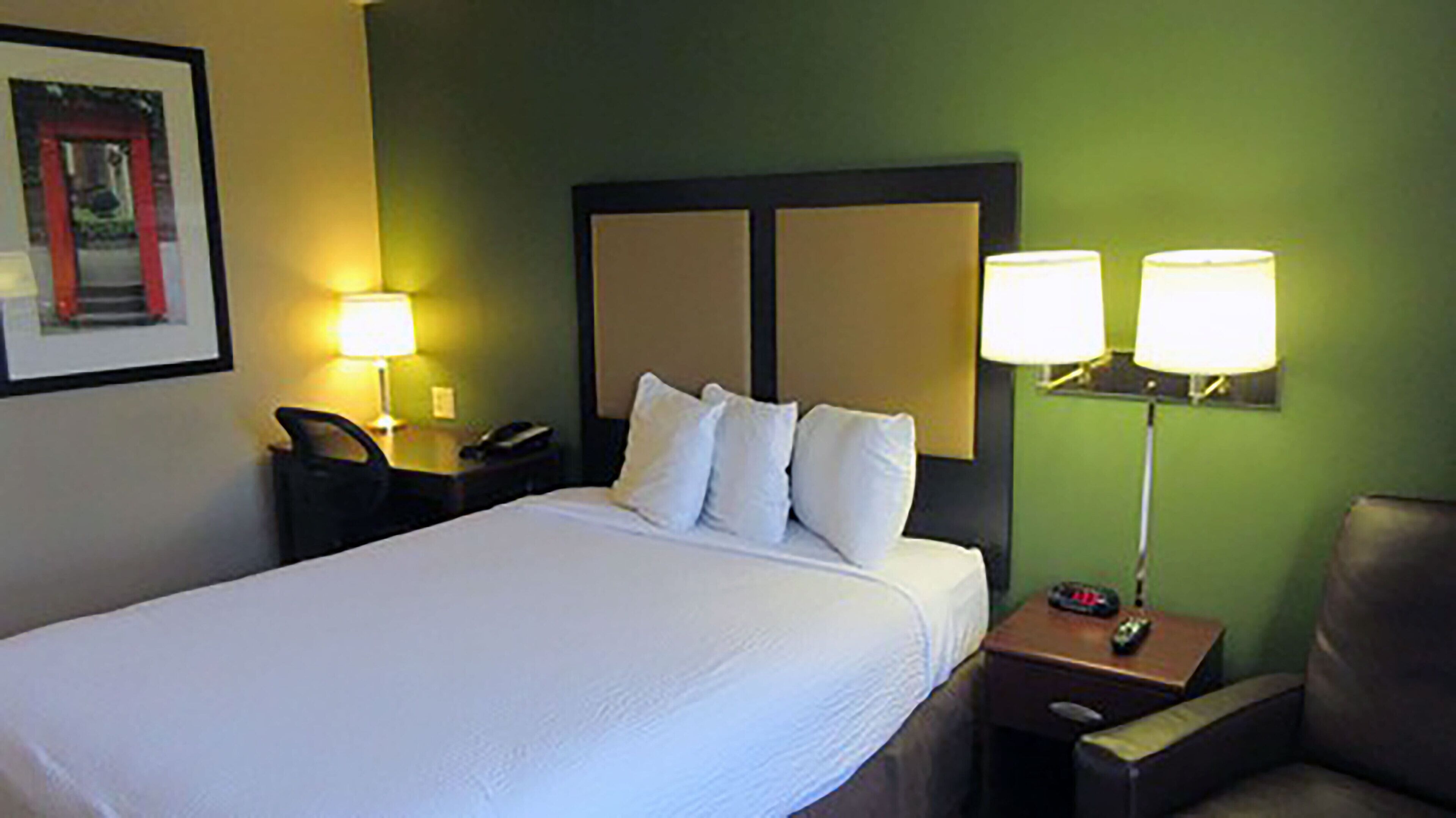 A hotel room with a large bed, two bedside lamps, a nightstand with a phone, and a chair.