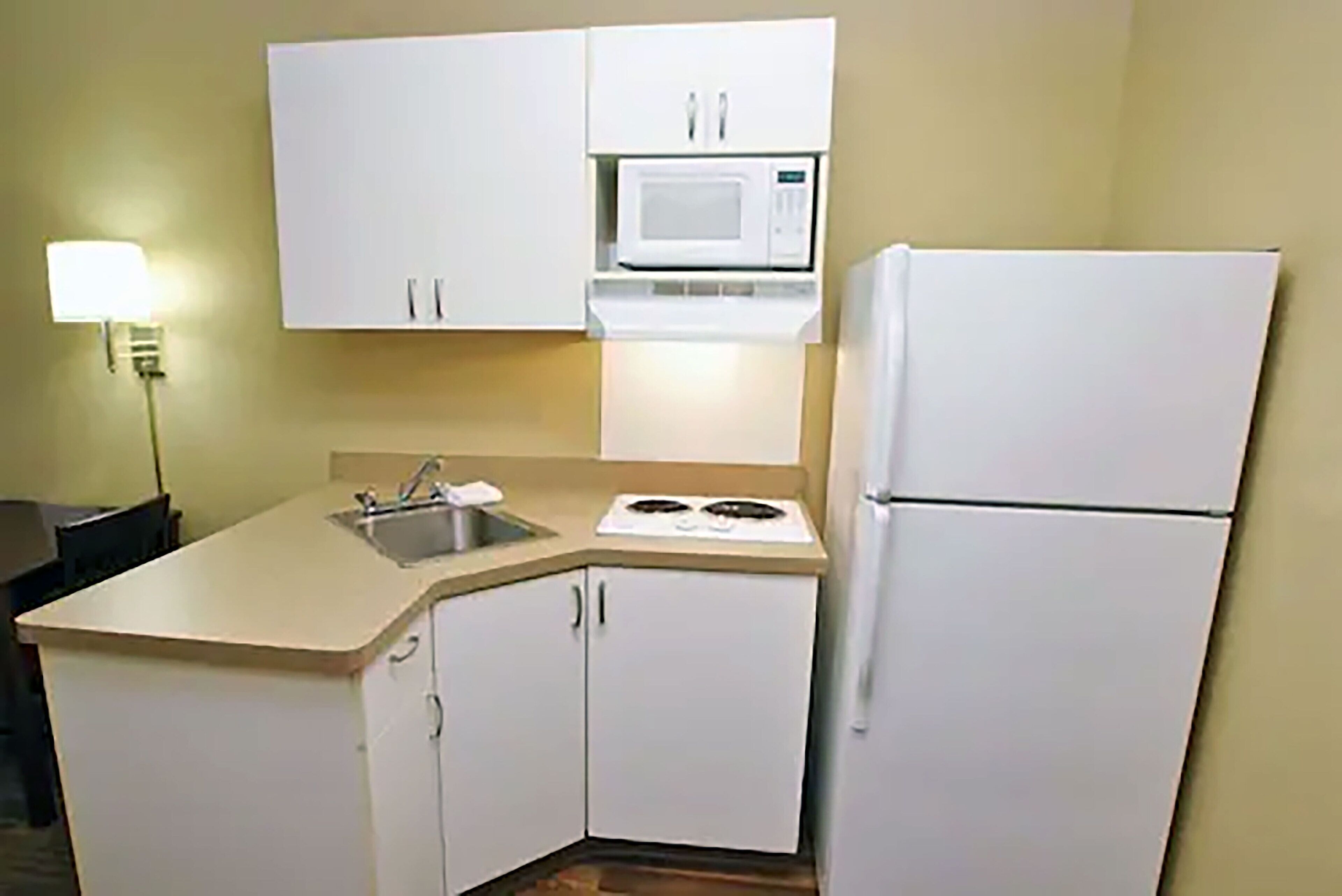 A compact kitchen with white cabinets, a microwave, a stove, and a refrigerator.