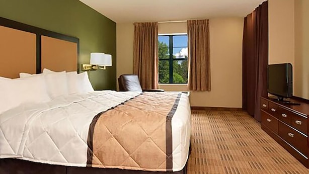 A hotel room with a large bed, a television, a desk, and a window with curtains.