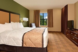 Habitación de hotel con una cama grande, televisión, escritorio y ventana con cortinas.