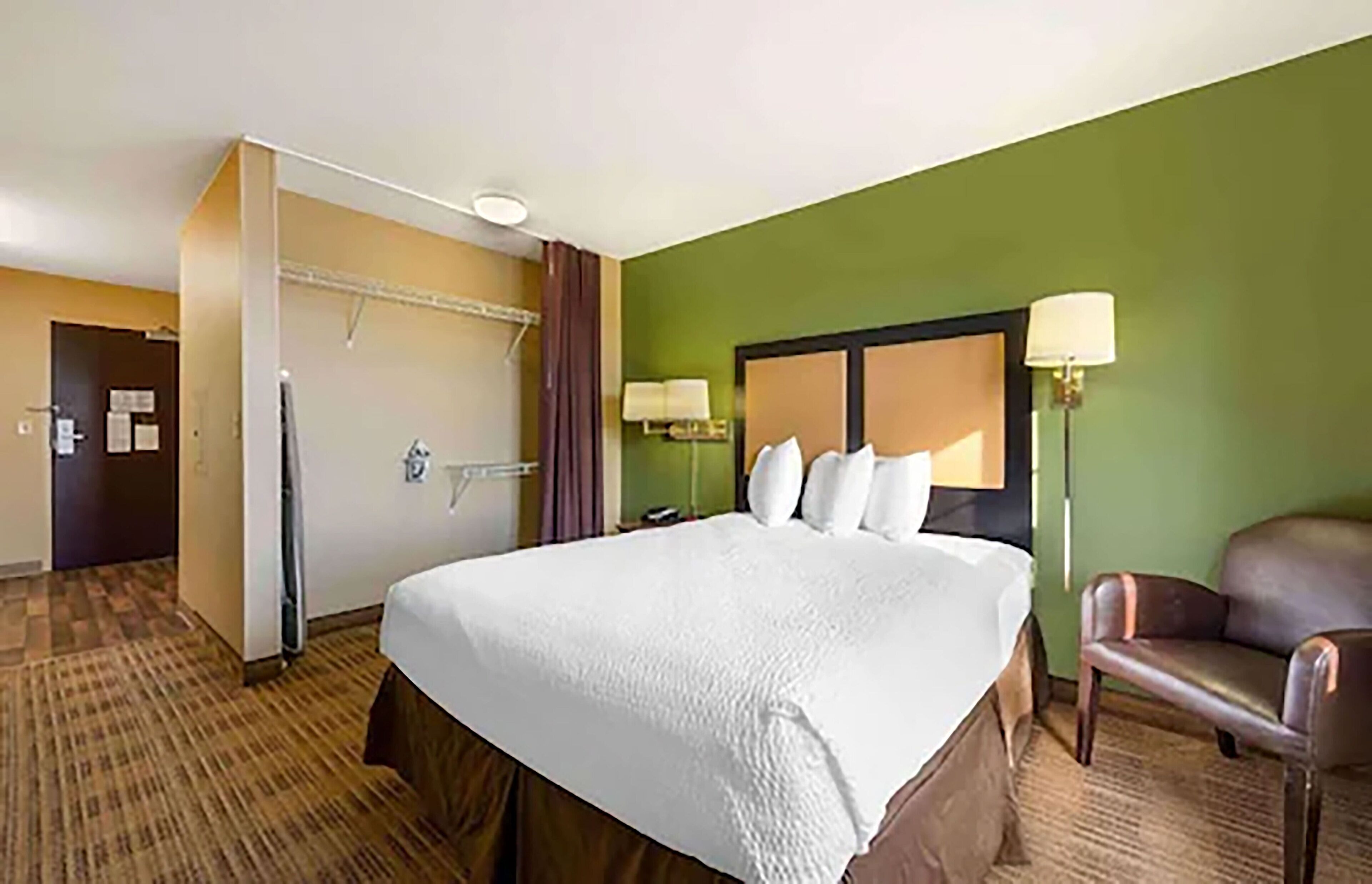 Una habitación de hotel con una cama grande, una silla, un escritorio y un armario.