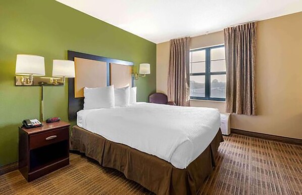 A hotel room with a large bed, two bedside lamps, a nightstand, a chair, and a window with curtains.