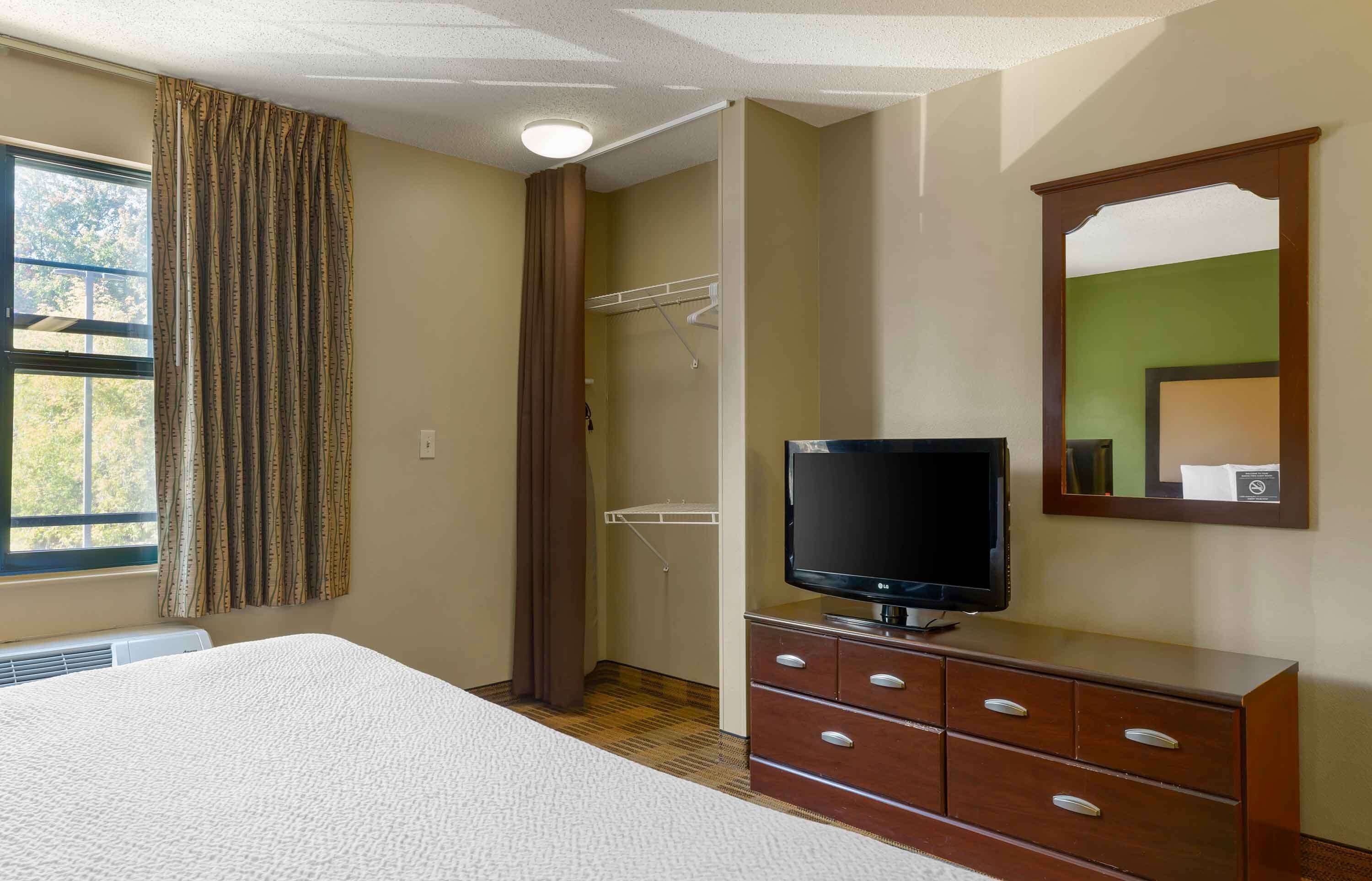 A hotel room with a bed, a TV on a wooden dresser, a closet, and a window with curtains.