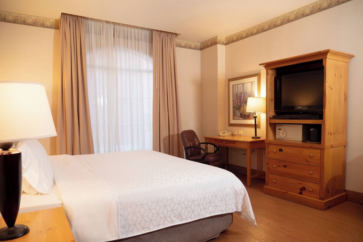 Una habitación de hotel con una cama, un escritorio, una silla, un televisor y una lámpara.