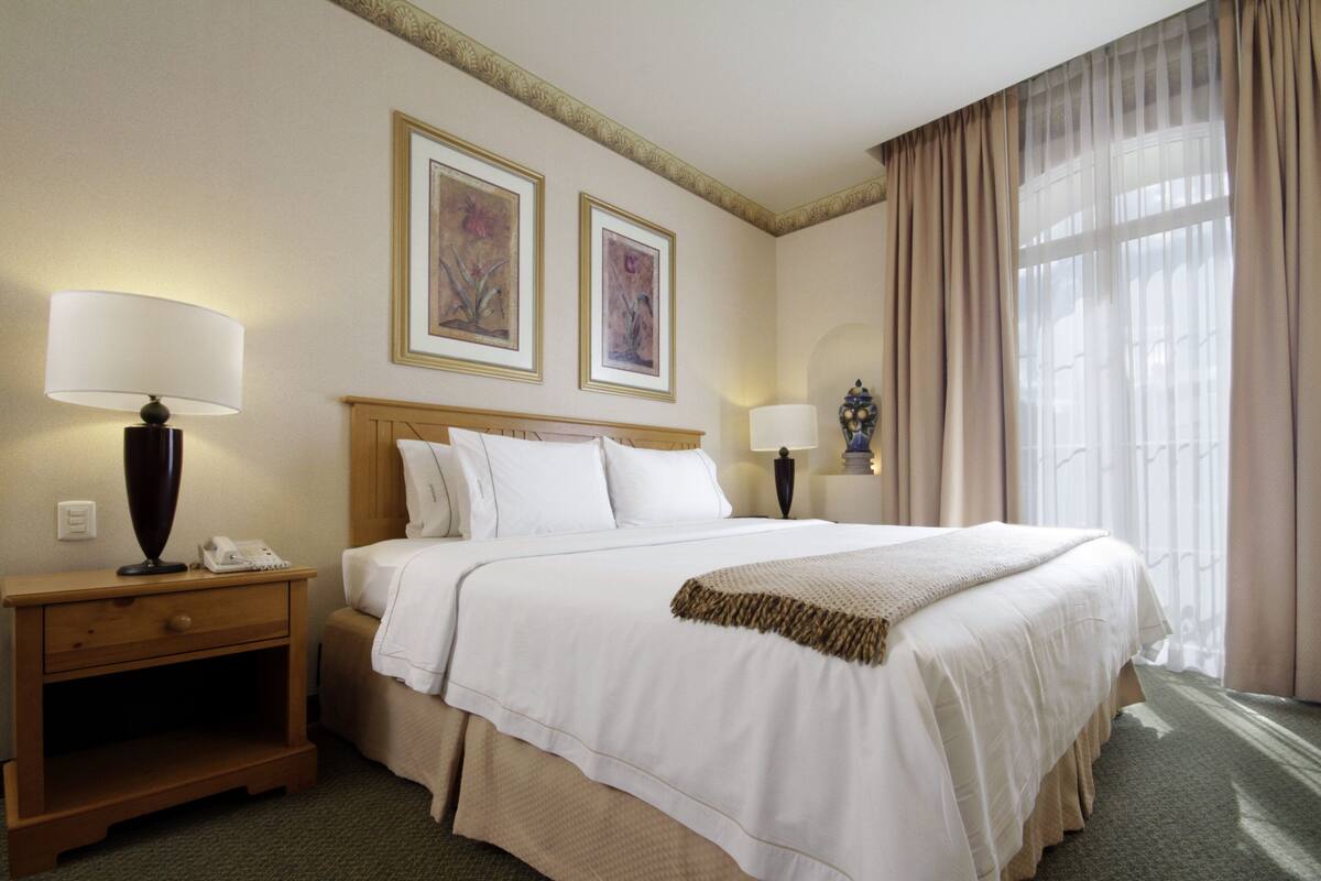 Una habitación de hotel con una cama grande, dos lámparas de noche, una mesita de noche y dos cuadros en la pared.