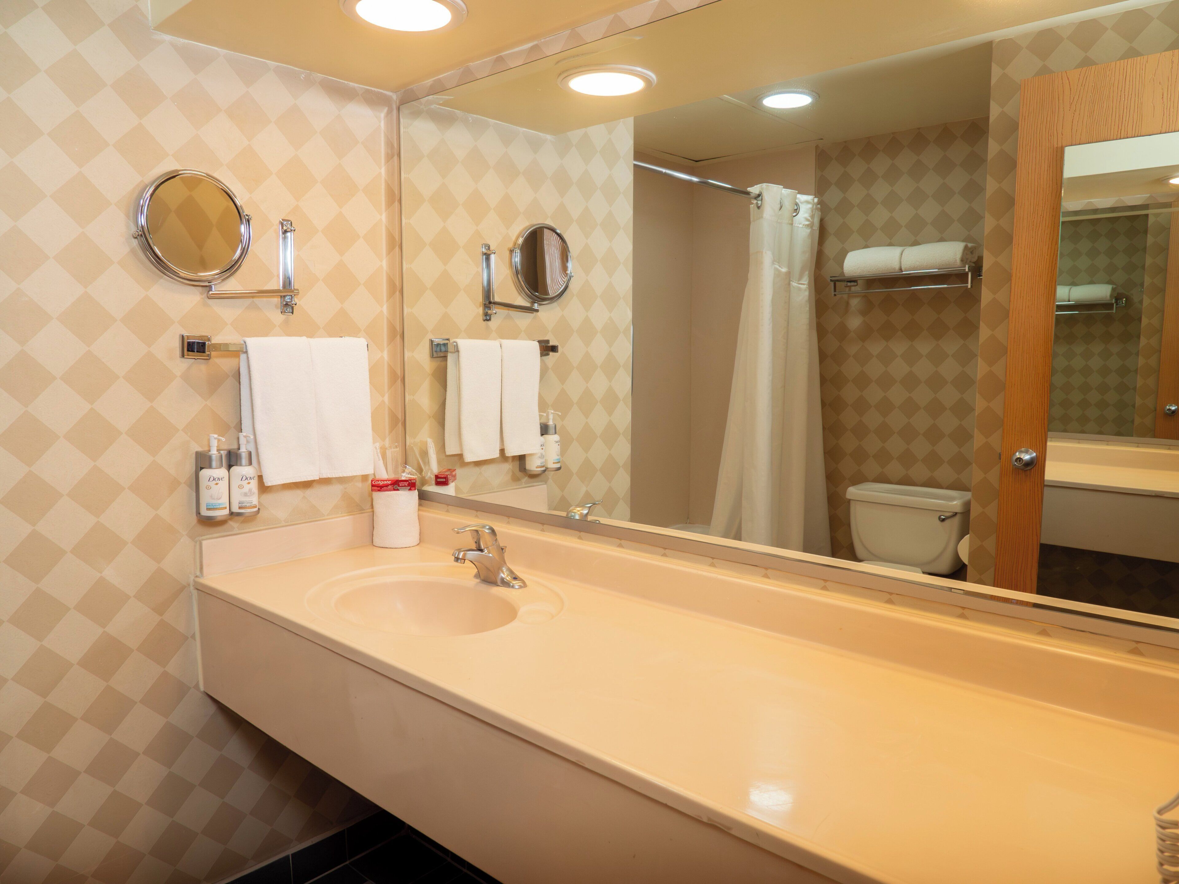 A bathroom with a sink, two mirrors, a toilet, and a shower curtain.