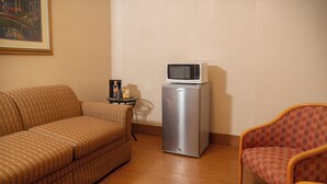 Un espacio habitable compacto con un sofá, una silla, una mesita con microondas y cafetera.