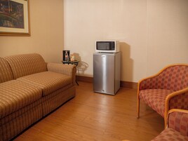 Un espacio habitable compacto con un sofá, una silla, una mesita con microondas y cafetera.