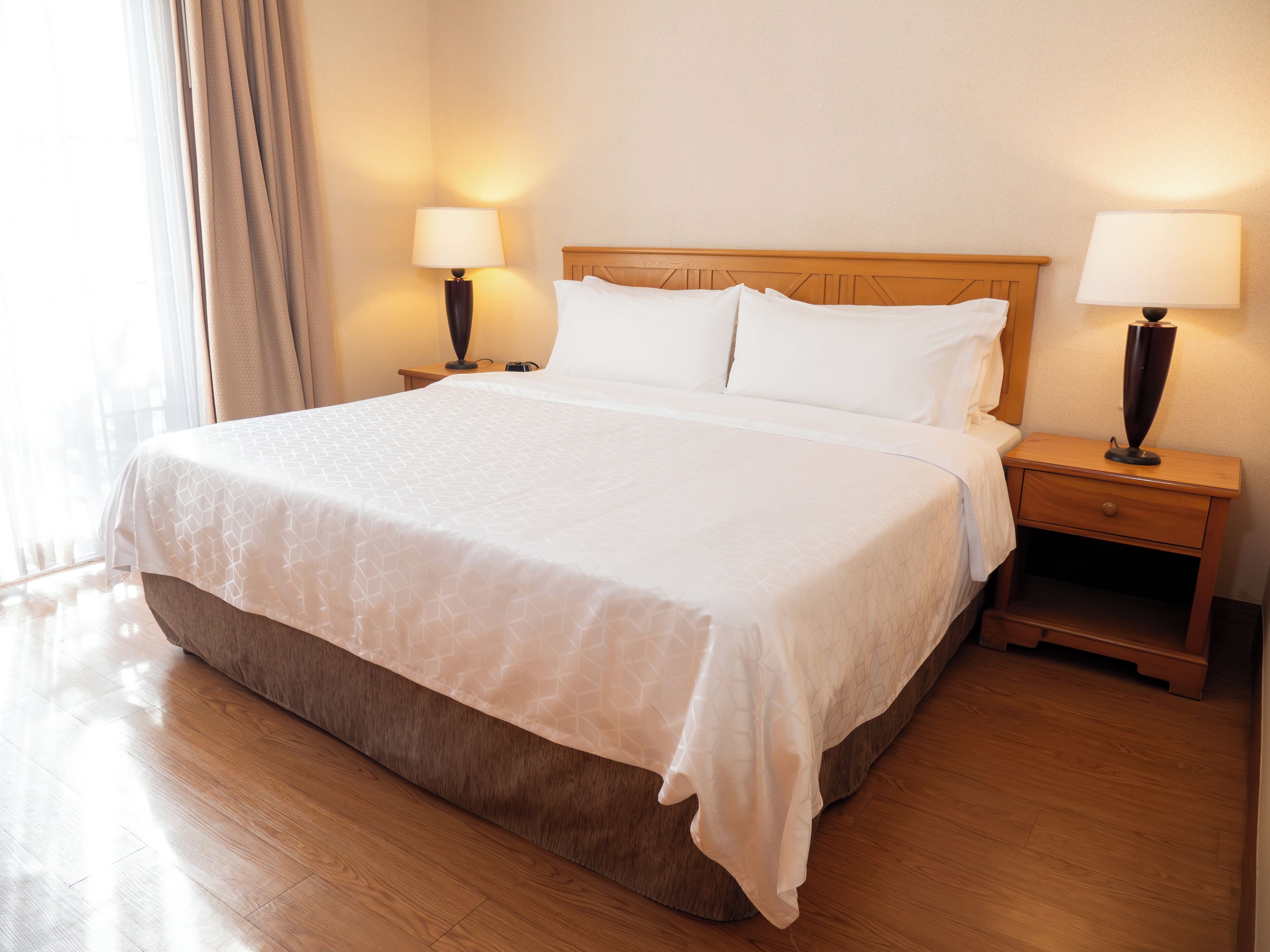 A neatly made bed with a wooden headboard, two bedside tables with lamps, and a wooden floor.