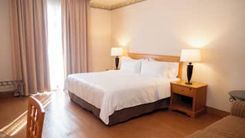Una habitación de hotel con una cama grande, dos mesitas de noche con lámparas, una silla de madera y una pequeña mesa redonda.