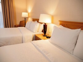 Una habitación de hotel con dos camas, una mesita de noche con lámpara y una ventana con cortinas.