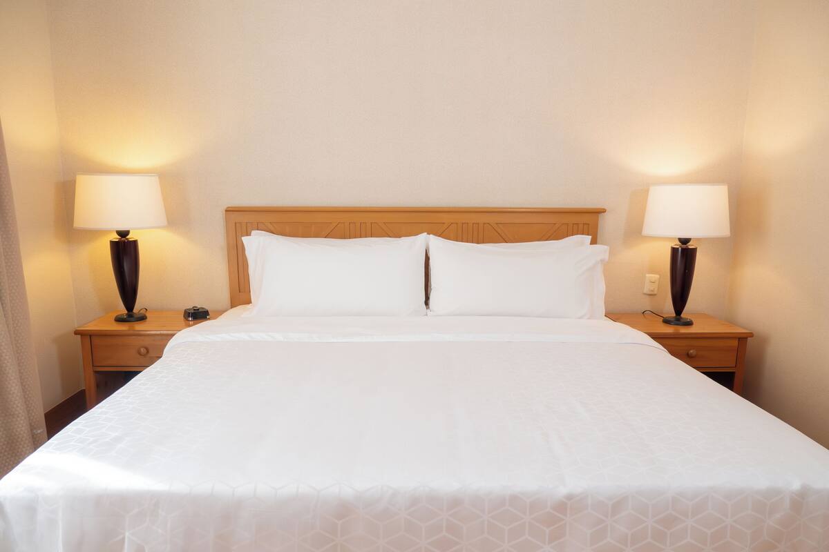 Una cama bien hecha con sábanas blancas y dos lámparas de noche sobre mesitas de madera.