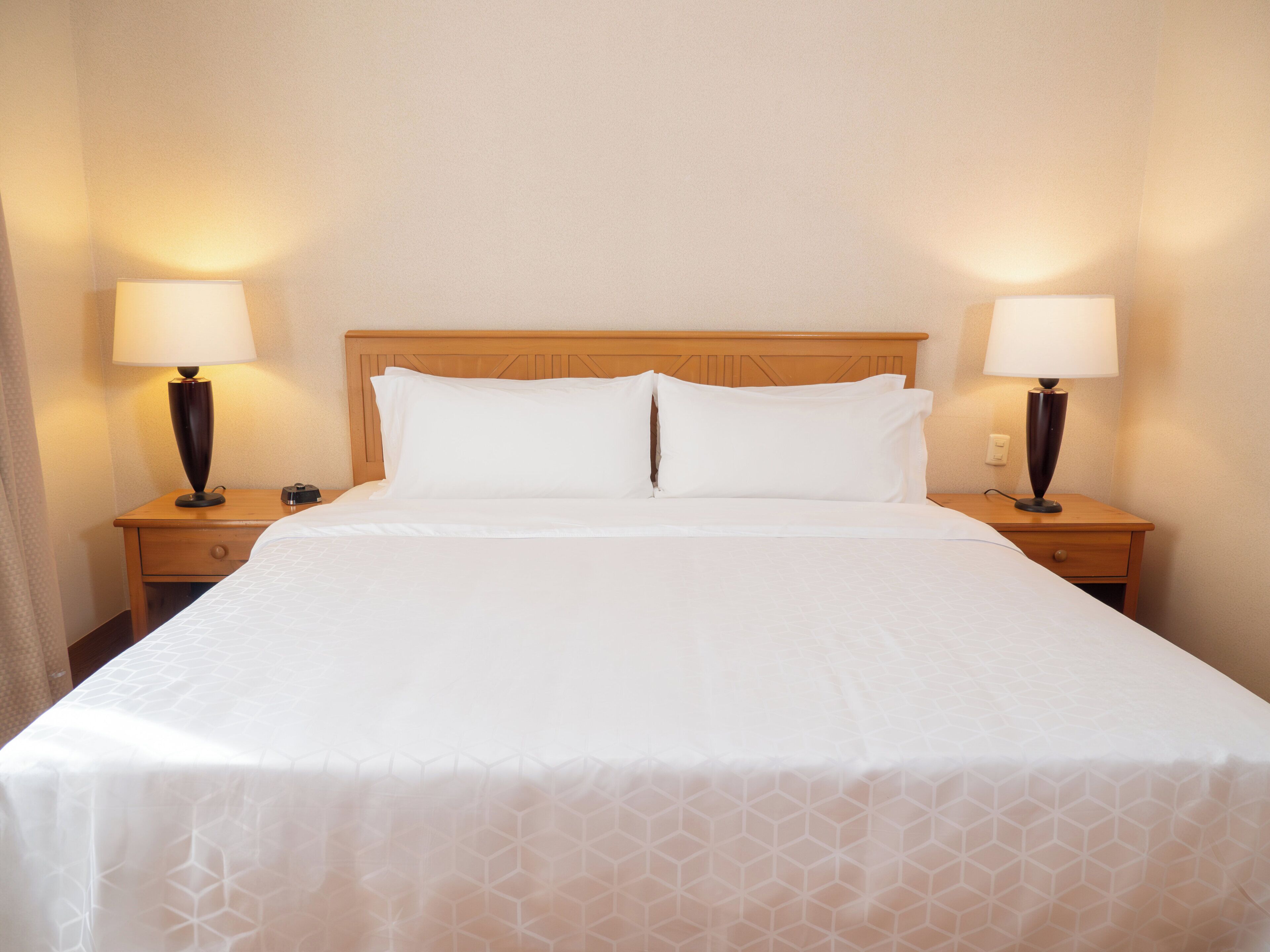 A neatly made bed with white linens and two bedside lamps on wooden nightstands.