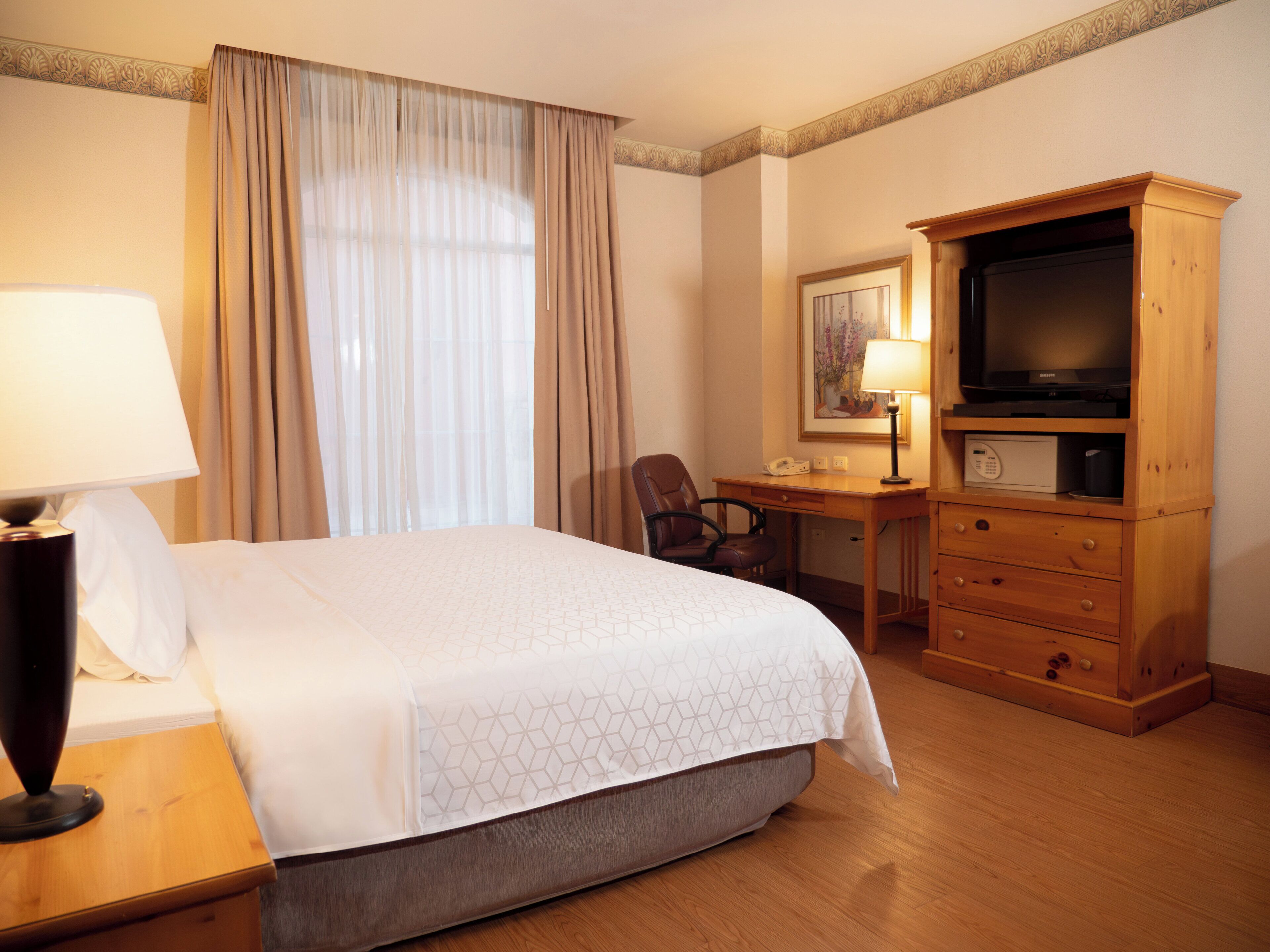 A hotel room with a bed, a desk, a chair, a television, and a lamp.
